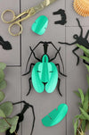 Green paper violin beetle craft by Assembli, showing a detailed, folded paper insect with vibrant green wings and intricate design.