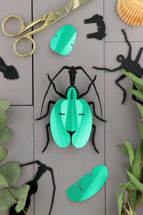 Green paper violin beetle craft by Assembli, showing a detailed, folded paper insect with vibrant green wings and intricate design.