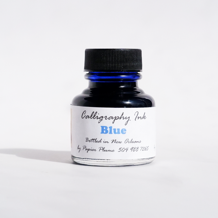 Blue bottled calligraphy ink by Papier Plume, featuring smooth, vibrant ink in a clear glass bottle for elegant writing.