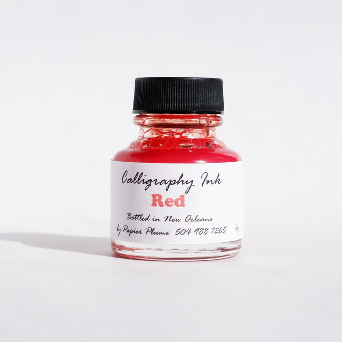 Red bottled calligraphy ink from Papier Plume, showcasing a glass bottle of vibrant red ink for artistic writing and calligraphy.