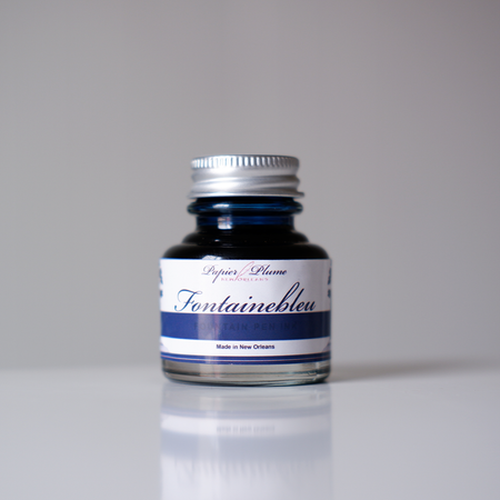 Bottle of Papier Plume Fontainebleu fountain pen ink with elegant blue ink in a glass container.