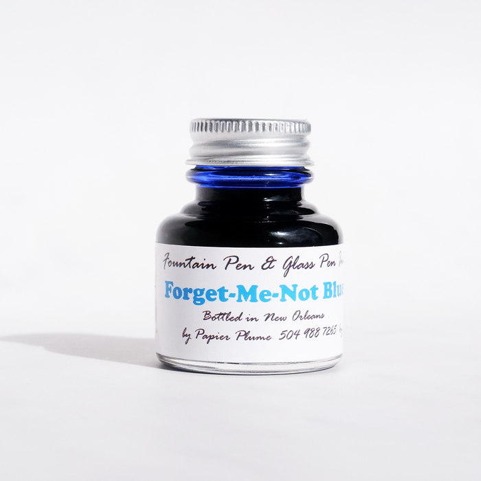 Papier Plume Forget-Me-Not Blue fountain pen ink in a glass bottle with vibrant blue ink visible inside.