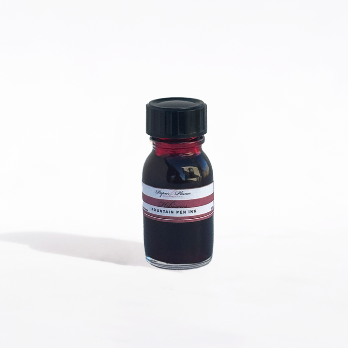 Papier Plume fountain pen ink bottle with hibiscus-colored ink in a clear glass container.