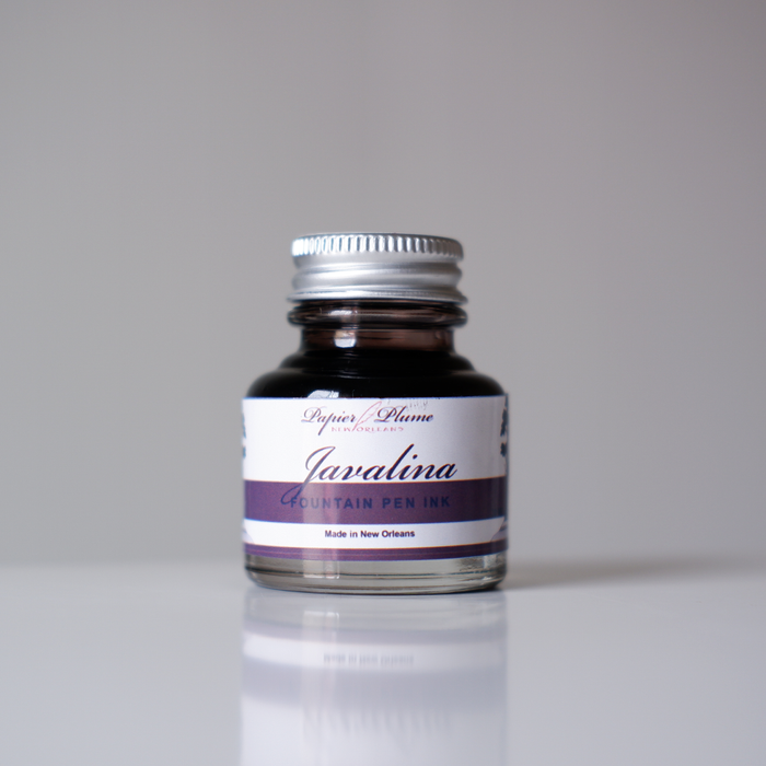Bottle of Papier Plume Javalina Fountain Pen Ink in a glass container with a black cap and label, showcasing vibrant ink inside.