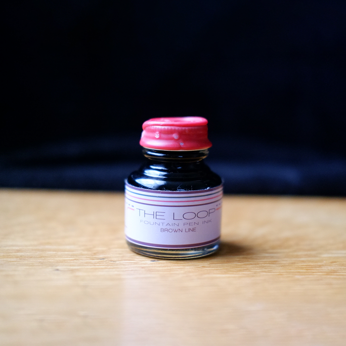 Papier Plume The Loop Series brown fountain pen ink bottle with a clear label and black cap, suitable for elegant writing.