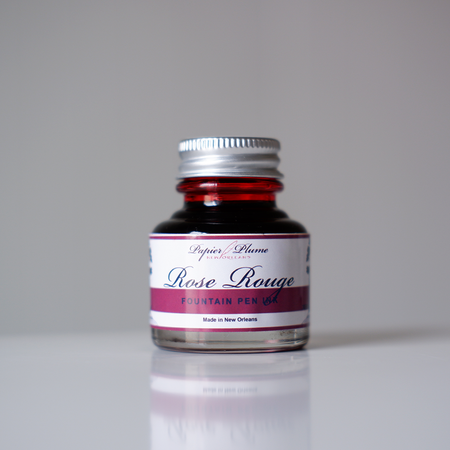 Papier Plume Rose Rouge fountain pen ink bottle with vibrant red ink in a clear glass container.