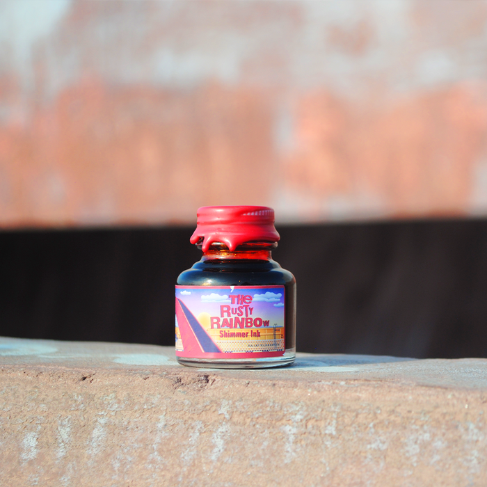 Papier Plume Rusty Rainbow shimmer fountain pen ink bottle with vibrant, iridescent orange and gold hues for writing or calligraphy.