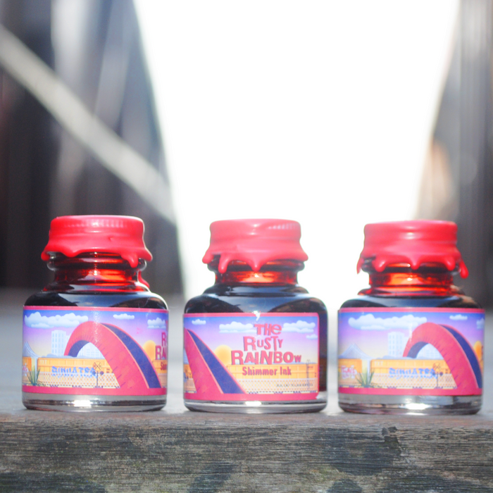 Papier Plume Rusty Rainbow shimmer fountain pen ink bottle with vibrant, multicolored ink visible in the glass container.