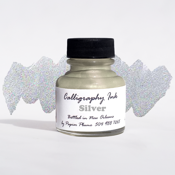 Bottled metallic silver calligraphy ink by Papier Plume with a sleek silver ink bottle and calligraphy nibs on a white background.