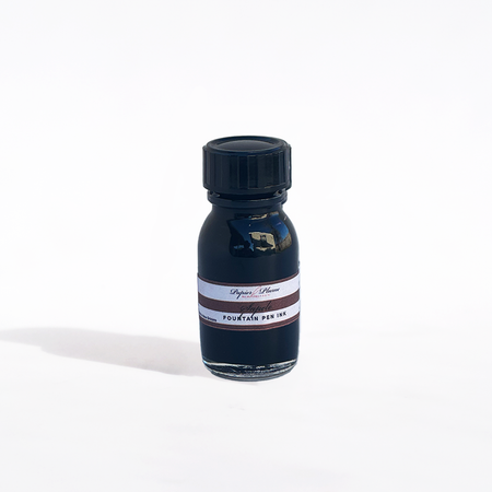Papier Plume fountain pen ink in Sapele color, featuring a glass bottle with dark amber liquid ink and a black cap.