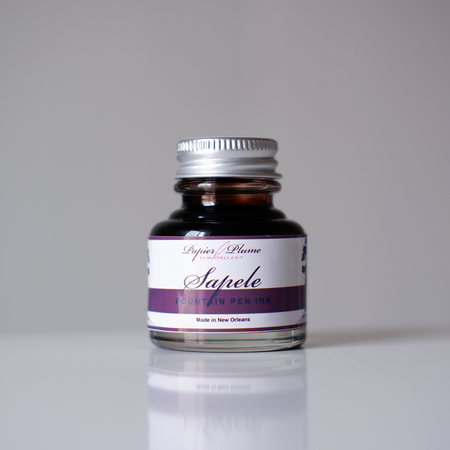Papier Plume Sapele fountain pen ink bottle with amber-colored ink in a glass container, ideal for fountain pen enthusiasts.