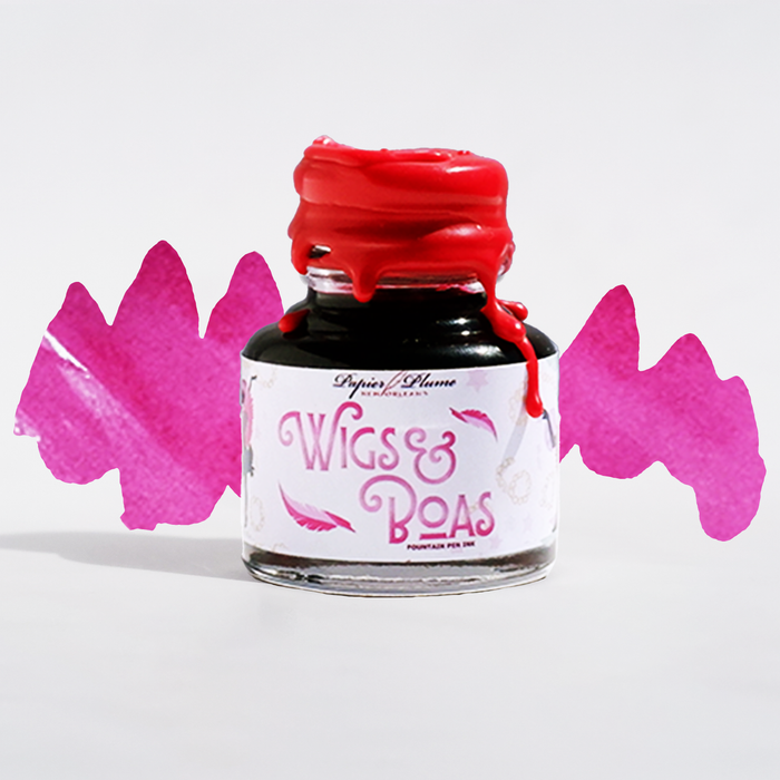 Image of Papier Plume New Orleans Collection fountain pen ink bottle with colorful wig and boa accessories in the background.