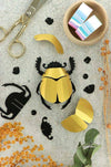 Colorful rainbow paper scarab beetle craft made from paper and plume, created by Assembli for artistic and decorative projects.