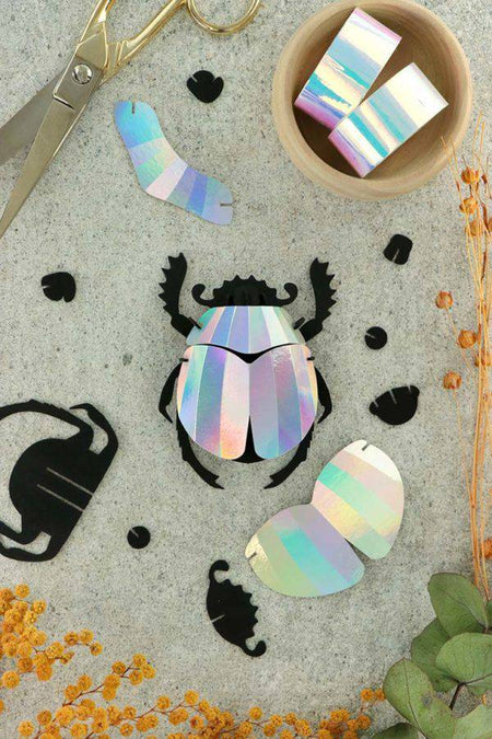 Colorful rainbow paper scarab beetle craft made from folded paper by Assembli, showcasing vibrant, intricate design.