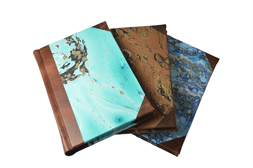 Handcrafted leather-trimmed journal with marbled paper and modern spine, featuring turquoise lined pages by Il Cartiglio.